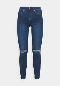 Jeans ajustados de color azul oscuro hechos de denim; presentan dos desgastes en las rodillas, bolsillos estándar y costuras en contraste.