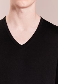 Maglione nero lavorato a maglia con scollatura a V, caratterizzato da una texture liscia e una vestibilità aderente, che mette in risalto uno stile minimalista.