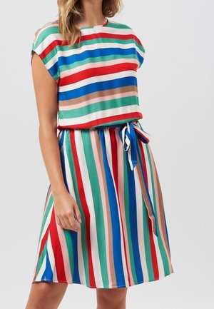 Femme portant une robe mi-longue avec des rayures horizontales sur le haut et des rayures verticales multicolores sur la jupe, nouée avec une ceinture à la taille.