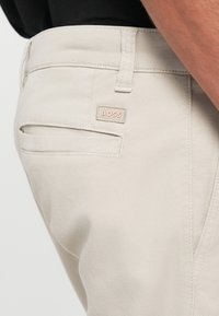 Pantalons en coton beige au design épuré, avec une étiquette de la marque BOSS sur la poche arrière et de subtils détails texturés.