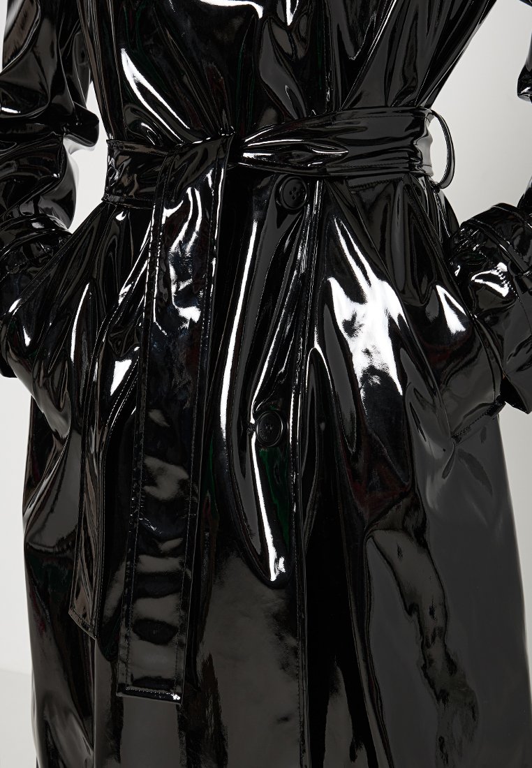 Schwarzer, glänzender Trenchcoat mit einem Gürtel, ausgestattet mit einer Knopfleiste und maßgeschneiderten Manschetten. Das Material hat ein hochglänzendes Finish und eine glatte Textur.