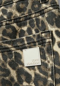 Tissu en denim imprimé léopard aux teintes de beige et de noir. Présente une étiquette blanche carrée avec le texte "Sofie Schnoor" sur la poche.