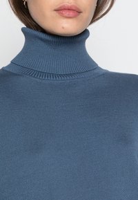 Pull au col roulé bleu clair avec une texture côtelée, présentant un col haut et un design près du corps. Tissu lisse avec des détails minimes.