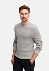 Pull en tricot gris clair avec un col rond et des poignets côtelés, associé à un pantalon noir. Le pull présente un motif texturé.