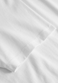 Tgană de bumbac alb cu o textură netedă, având un margine tivită și detalii de cusătură subtile.