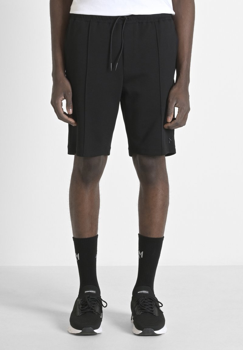 Pantaloni sportivi neri con cintura elastica e lacci, caratterizzati da due pieghe frontali e un sottile dettaglio del logo sul lato.