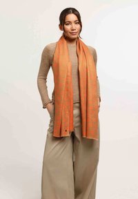 Écharpe orange avec un motif subtil de léopard, fabriquée en matériau doux, drapée confortablement autour du cou du modèle.
