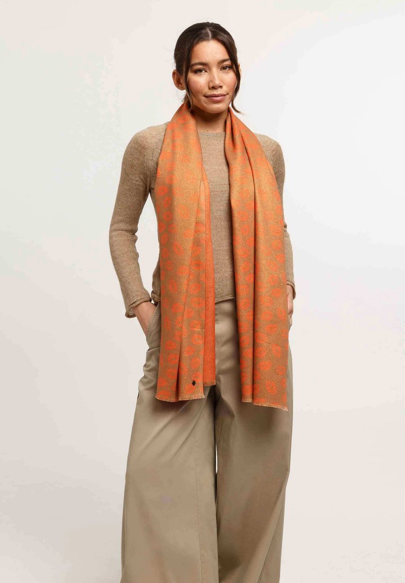 Écharpe orange avec un motif subtil de léopard, fabriquée en matériau doux, drapée confortablement autour du cou du modèle.