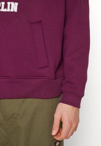 Bordeaux hoodie met een geribbelde onderrand en mouwen, met een voorzak. Textuurstof, weergegeven met olijfgroene cargobroeken.