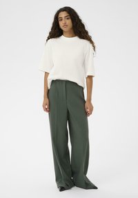 Off-white, oversize póló és sötétzöld, bő szárú nadrág. Az anyag simának tűnik, egyszerű dizájnnal és minimalista részletekkel.