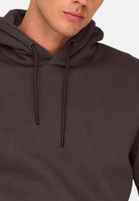 Felpa con cappuccio grigio scuro, dal tocco morbido, con tasca a marsupio e dettagli neri sui lacci del cappuccio. Design semplice e casual.