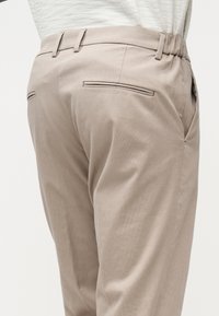 Beige bukser med beltehemper, baklommer med åpning og sidelommer, båret med en innslogan hvit teksturert topp.