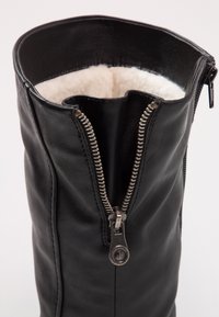 Czarne skórzane buty z wyraźnym srebrnym zamkiem błyskawicznym i miękkim, wyściełanym białym wykończeniem u góry. Gładka tekstura i elegancki design.