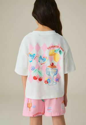 Barn iført hvid T-shirt og lyserøde shorts med farverige sommermotiver inklusive kirsebær, solbriller, is og citroner.