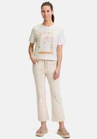Katoenen T-shirt in off-white met een palmboom grafiek, gecombineerd met lichtbeige flared jeans en tan platform sandalen.