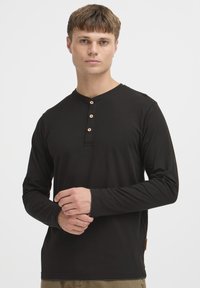 Zwarte lange mouwen shirt met een ronde hals, vijf knopen en een label aan de zoom, gemaakt van zacht materiaal met een gladde textuur.