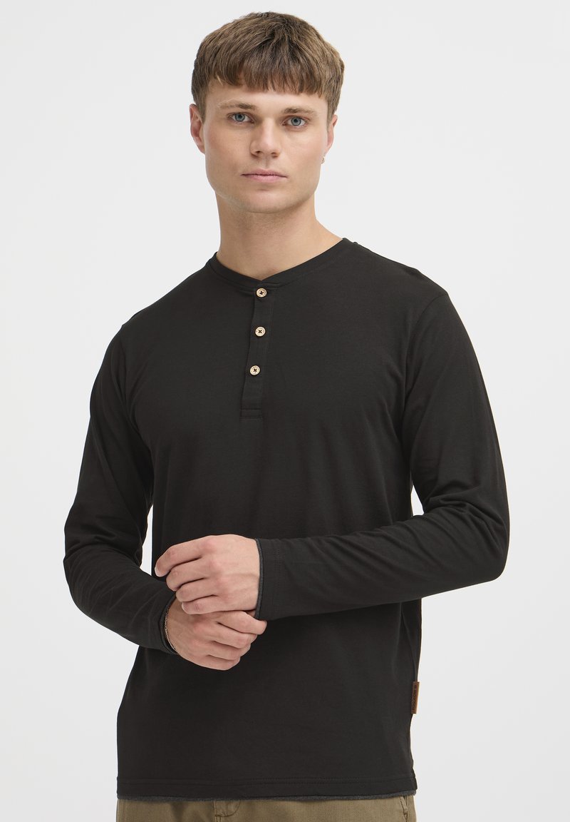 Zwarte lange mouwen shirt met een ronde hals, vijf knopen en een label aan de zoom, gemaakt van zacht materiaal met een gladde textuur.