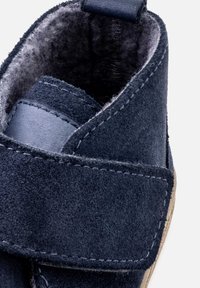 Tengerészeti kék velúr bokacsizma bőr díszítéssel, tépőzáras pánttal, puha bélésű belső résszel és bézs talppal.