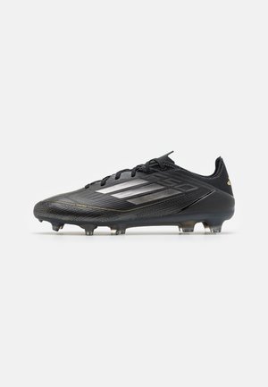 Black soccer cleat with a textured surface, featuring three silver stripes and subtle gold accents. Designed for performance with a lightweight build.