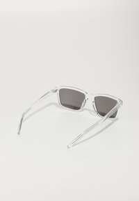 Lunettes de soleil carrées et transparentes avec des verres foncés. Des branches fines s'étendent du cadre. Design minimaliste sans motifs visibles.