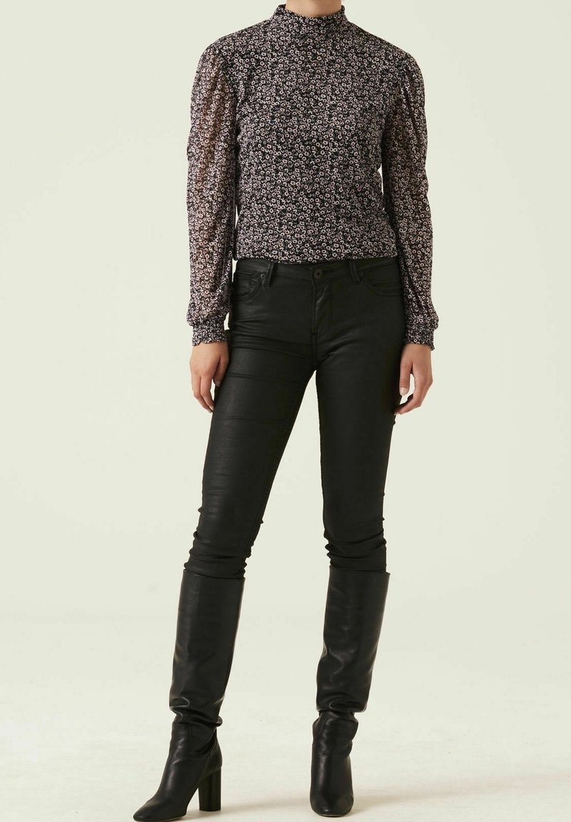 Svart blommig blus med långa ärmar och hög krage, kombinerad med åtsittande svarta läderbyxor och knähöga svarta stilettklackar.