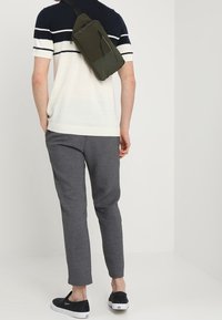 Šedé zúžené kalhoty, krátký rukáv ve navy a bílé pruhy, olivově zelená crossbody taška, nošeno s černými nazouvacími botami.