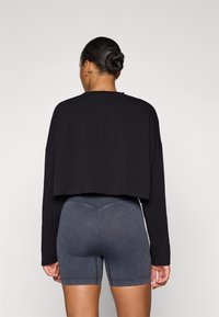 Zwarte cropped langemouwen top met een ronde hals, gecombineerd met donkergrijze high-waisted shorts die een gladde, rekbare textuur hebben.