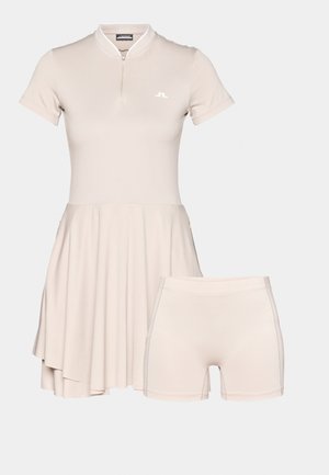 Beige dress with short sleeves and a zippered collar, featuring a flared skirt and matching beige shorts, made of smooth, stretchy fabric.