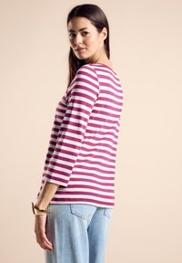 Maglietta a maniche lunghe a righe in cotone rosa e bianco, con scollatura rotonda e vestibilità rilassata. Abbinata a jeans in denim azzurro chiaro.