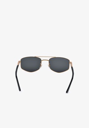 Lunettes de soleil avec des verres rectangulaires foncés, une monture fine en métal doré, des embouts de branches noirs et des plaquettes de nez réglables sur fond blanc.