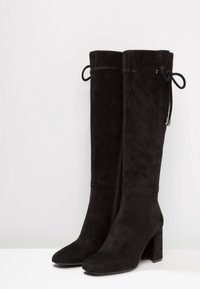 Botas altas de ante negro con punta cuadrada, tacón grueso, cierre de cremallera lateral y detalle de cordones ajustable en la parte superior.