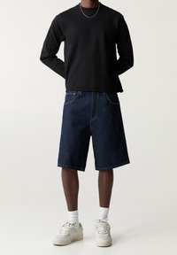 T-shirt noir à manches longues, short en denim bleu et baskets blanches avec des accents gris. Design simple, coutures visibles et coupe décontractée.