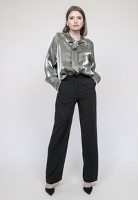 Blouse en satin vert avec un nœud attaché au col, associée à un pantalon noir taille haute et des escarpins noirs à bout pointu.