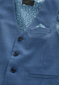 Sinine vest tekstuurse kangaga ja lillemustrilise voodriga. Varustatud kolme nupu, rinnanõtme ja voltidega taskurätikuga.