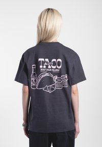 Mörkgrå bomullst-shirt med en rosa grafisk design på baksidan, som föreställer tacos, het sås och drycker i en lekfull layout.