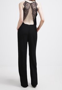 Combinaison noire avec un dos en dentelle, sans manches, et un pantalon à jambes larges. Dos découvert avec un délicat détail en dentelle. Fermeture zippée au dos.