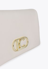 Primo piano di una borsa bianca con logo dorato sul davanti, che evidenzia il suo design elegante e moderno.