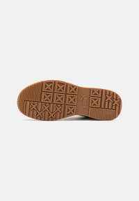 Rubber shoe sole with textured patterns, featuring a series of crosses and grooves, in a light brown color with branding.