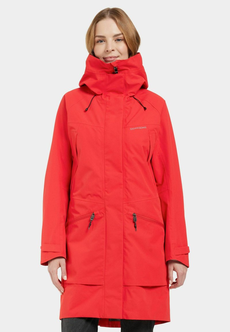 Manteau imperméable rouge avec un col haut, une capuche ajustable, des poches zippées et une coupe décontractée. Présente une finition mate et un tissu résistant.