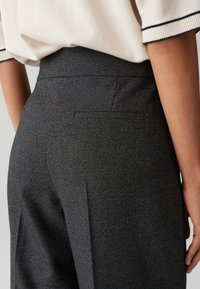 Zwarte op maat gemaakte broek met een gestructureerde stof. Hoge tailleband, één achterzak en een recht model. Geaccentueerd met een subtiele glans.