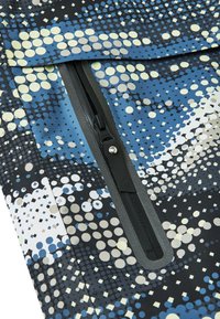 Tejido multicolor con patrones circulares en azul, negro y blanco; incluye una cremallera con un tirador negro, sobre un fondo texturizado.