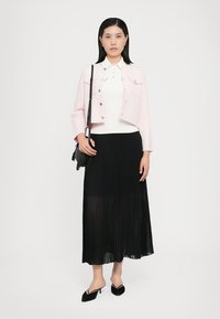 Světle růžová zkrácená bunda, bílý přiléhavý top a černá plisovaná maxi sukně. Černé lodičky a malá černá kabelka dokončují celý outfit.