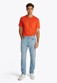 Tricou de culoare portocaliu aprins, cu mâneci scurte și buzunar la piept, asortat cu blugi albaștri deschiși și adidași albi, caracterizat printr-o croială casual și o textură moale.