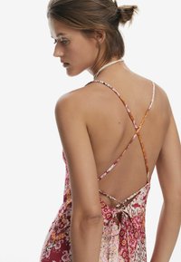 Vestido maxi con un patrón floral en tonos de rosa y naranja. Presenta tirantes delgados en cruz y una espalda atada para un ajuste ajustable.