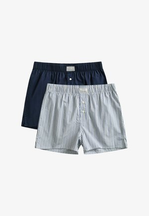 Deux caleçons pour hommes, l’un uni bleu marine et l’autre blanc à rayures bleues, tous deux avec des ceintures élastiques et des boutons à l’avant.