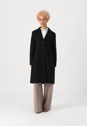 Black wool coat with a notched lapel, two front buttons, and side pockets. Simple design, mid-length, worn over a light collared shirt and trousers.