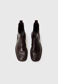 Botas de cuero marrón oscuro hasta el tobillo con detalles en patrón de cocodrilo, paneles laterales elásticos y una suela texturizada para mayor agarre.