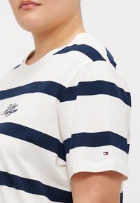 Hvid bomulds T-shirt med marineblå vandret striber, en rund halsudskæring og et lille logo på brystet. Korte ærmer med kontrastfarvede detaljer.