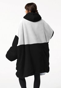 Schwarze und weiße übergroße Kapuzen-Decke mit einer weichen Textur, die ein geteiltes Farbd design aufweist; der untere Teil ist schwarz und der obere Teil ist weiß.