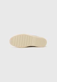 Suola di sneaker in gomma beige chiaro con texture rigata e linee orizzontali. Nome del marchio "HACKETT" impresso vicino al tallone.